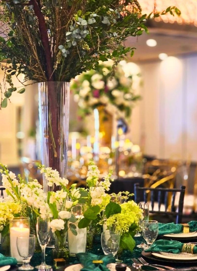 Green & white tall centerpiece: Fresh white blooms, lush greenery, and organic branch arrangements against deep emerald linens — fresh flowers for weddings in Metro Detroit that make every table feel like a garden in full bloom.