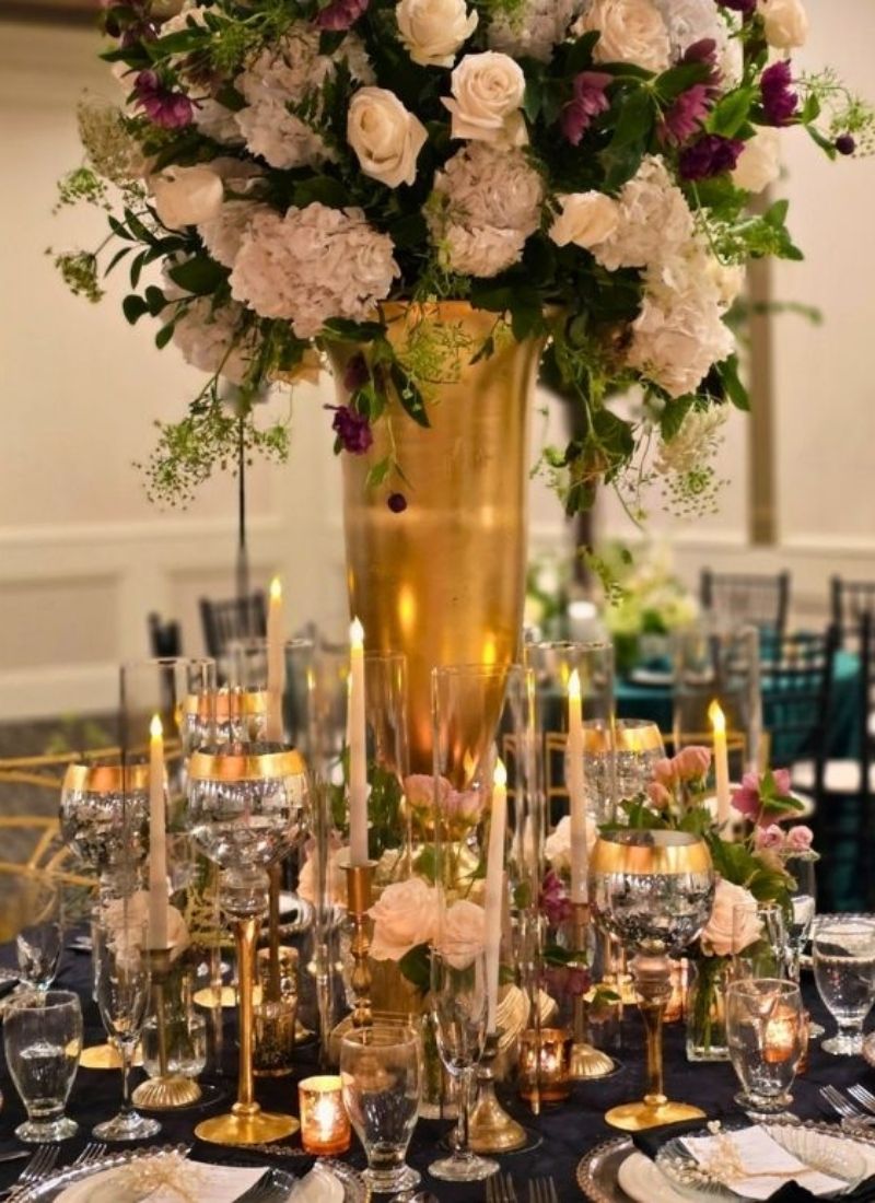 White & gold tall centerpiece with candlelight: White hydrangeas, blush roses, and deep purple accents in a gold stand arrangement surrounded by candlelight — the signature drama of Bridal Insignia's fresh flower centerpieces in Metro Detroit.