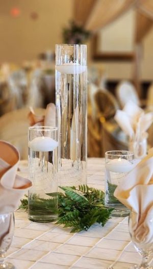 Elegant wedding centerpieces in Metro Detroit by Bridal Insignia — glass cylinder vase with floating candle on a champagne pintuck table cover with greeneries